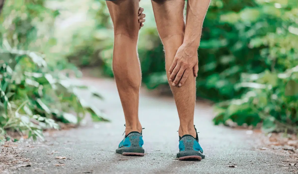 Close-up of a runner holding their calf, representing an athletic injury, muscle strain, or chronic leg pain that requires treatment.
