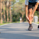 Young fitness man holding his sports leg injury. muscle painful during training. Asian runner having calf ache and problem after running and exercise outside morning. sport and healthy concepts leg pain